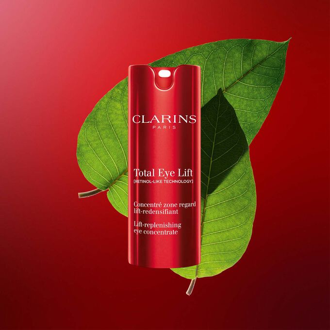 Imagem da embalagem do creme antienvelhecimento para os olhos Clarins Total Eye Lift com folhas de harungana sobre um fundo vermelho escuro.