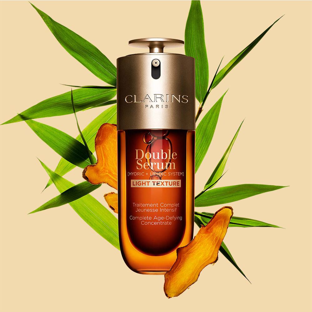 Um frasco de 50 ml de Clarins Double Serum Light Texture entre folhas de curcuma e cana-do-reino sobre um fundo laranja.
