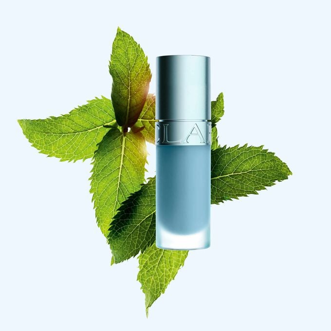 Imagem de Clarins Lip Comfort Oil com o novo efeito refrescante e acabamento brilhante, em frente a hortel&atilde; para destacar o seu ingrediente principal.