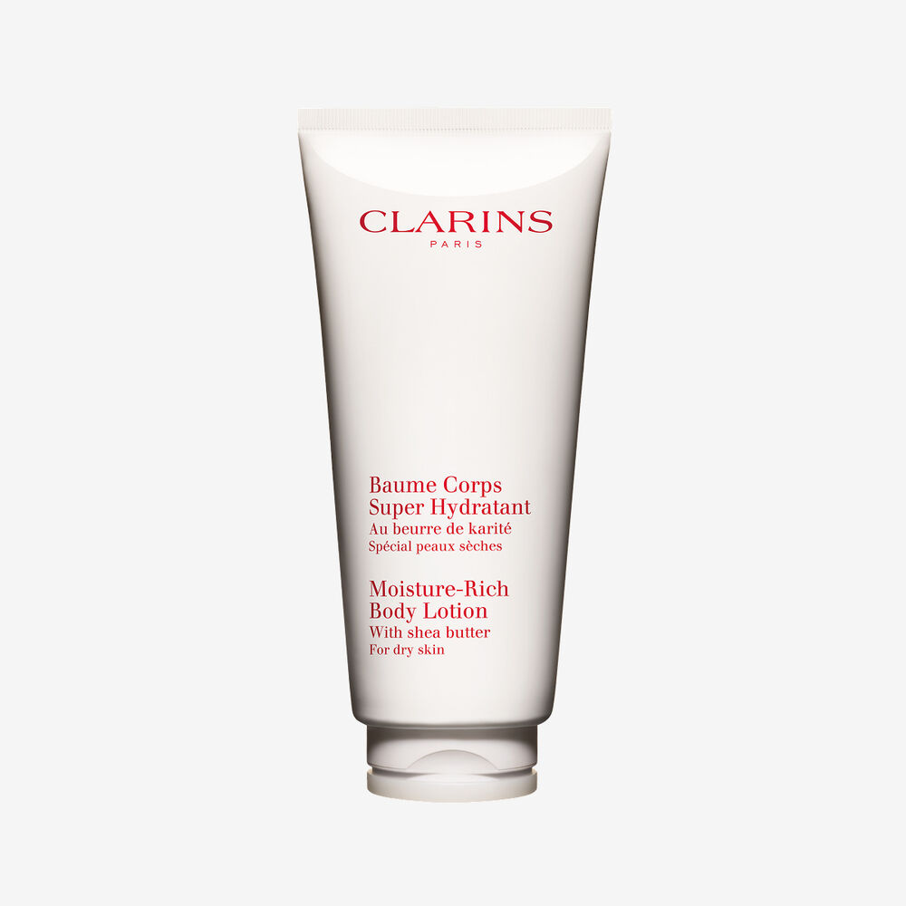 Embalagem de Clarins Baume Corps Super Hydratant apresentada junto a frutos de manteiga de karit&eacute; natural sobre um elegante fundo branco.