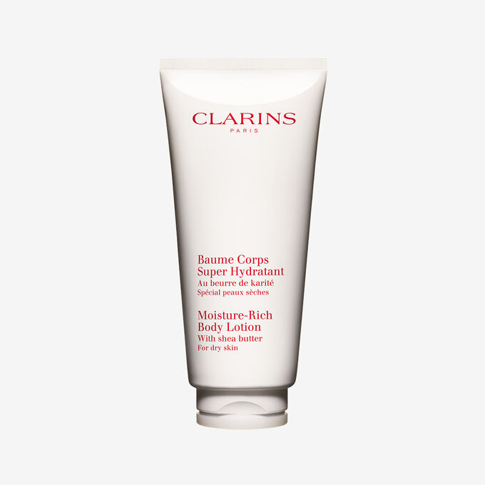 Embalagem de Clarins Baume Corps Super Hydratant apresentada junto a frutos de manteiga de karit&eacute; natural sobre um elegante fundo branco.