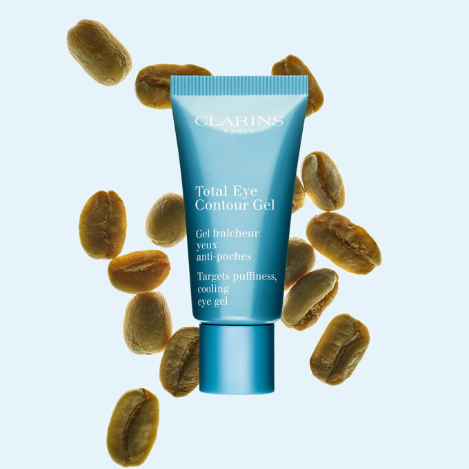 Embalagem de gel para o contorno dos olhos Total Eye Contour Gel Clarins, apresentado com gr&atilde;os de caf&eacute; verde sobre um fundo azul-claro suave.