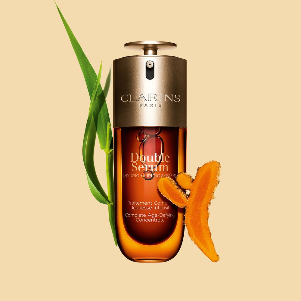 Imagem de Clarins Double Serum apresentado em frente dos seus ingredientes, incluindo curcuma, sobre um fundo dourado