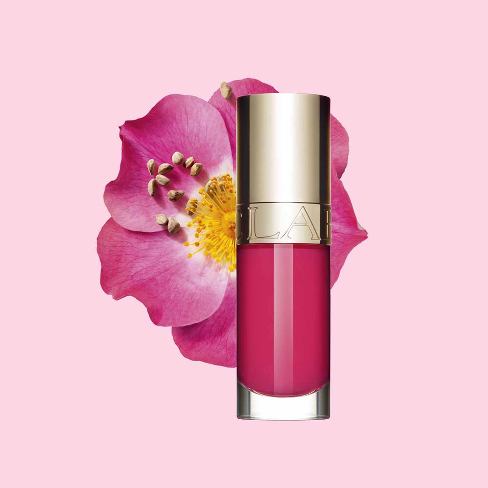 Imagem do produto óleo cor-de-rosa para lábios Clarins à frente de uma flor rosa mosqueta sobre um fundo branco