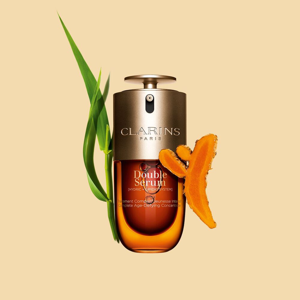 Imagem de Clarins Double Serum apresentado em frente dos seus ingredientes, incluindo curcuma, sobre um fundo dourado
