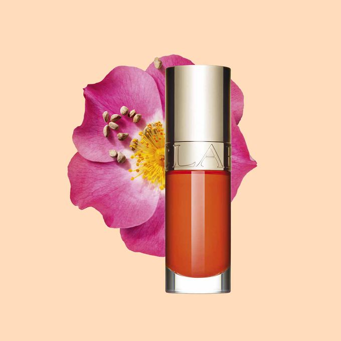 Imagem do produto &oacute;leo laranja escuro para l&aacute;bios Clarins &agrave; frente de uma flor rosa mosqueta sobre um fundo branco